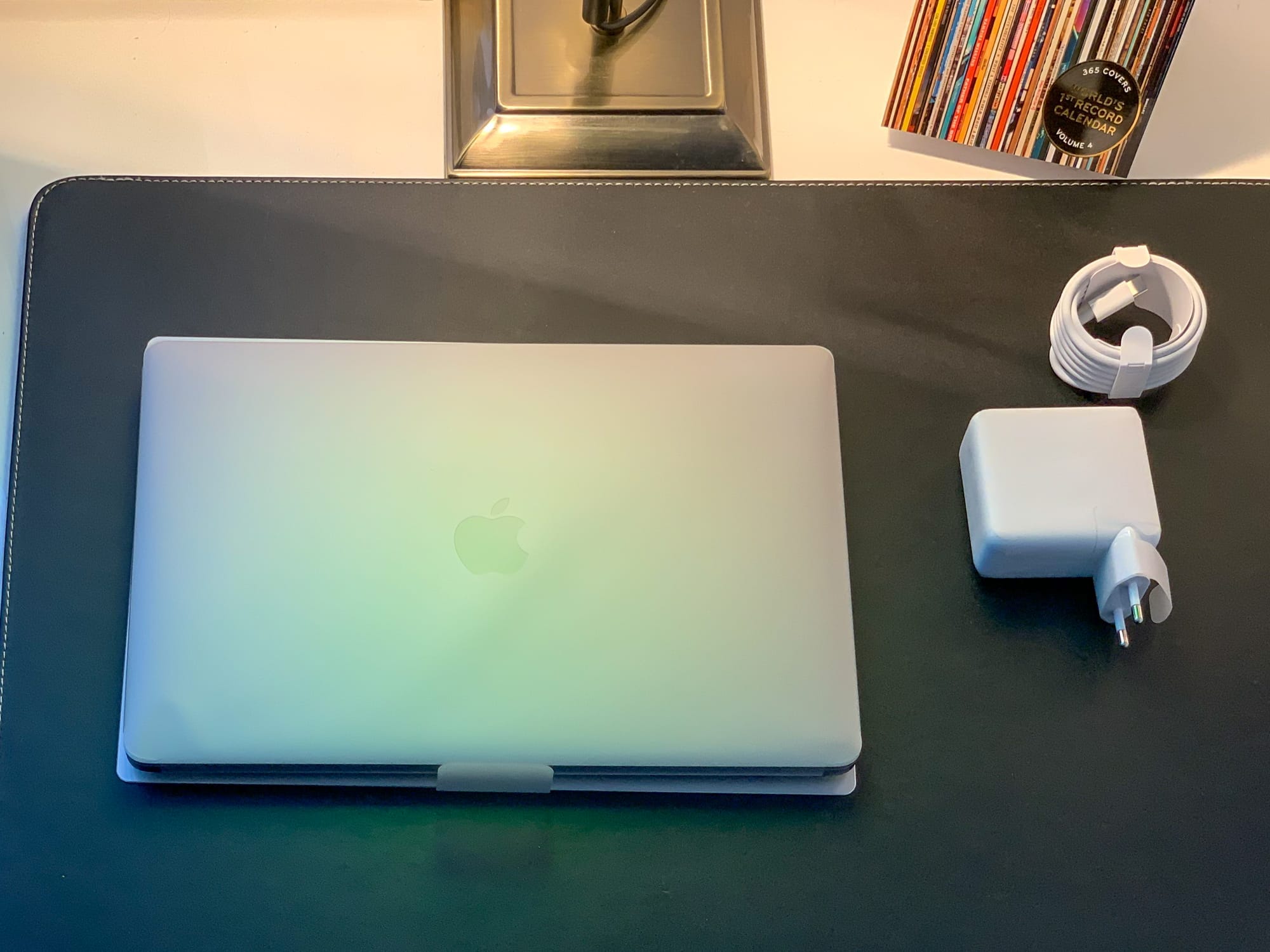Ein graues MacBook liegt zugeklappt auf einem Schreibtisch, rechts davon liegen Netzteil sowie das USB-C-Kabel.